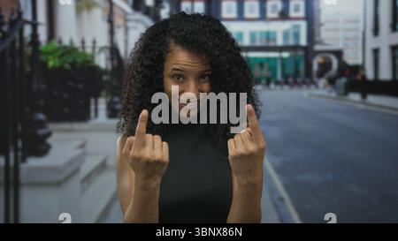 Young hispanic woman beckons with both hands forward on quiet city street; invitation greeting friendly. Stock Photo