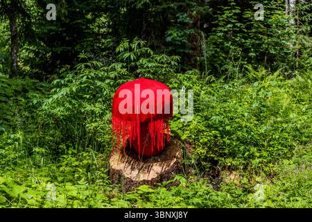 The thread sculpture by German artist Marion Strunk here forms a vivid red, mushroom- or tassel-shaped structure made of red wool on a tree stump amid lush greenery on the Gerschnialp near Engelberg. Long, hanging strands surround the domed top. An appreciation of nature runs like a red thread through the work, part of the 2025 exhibition "Outlook – Insight" on the Gerschnialp Land Art Trail, Engelberg, Canton of Obwalden, Switzerland. Stock Photo