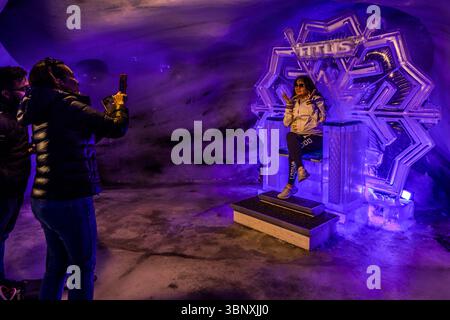 The Titlis Glacier Grotto is a tourist attraction at an altitude of over 3,000 metres, located directly at the Titlis cable car summit station. The grotto consists of an approximately 150-metre-long, artificially created passageway that leads around 20 metres below the surface of the glacier. The tunnel features photo spots such as a throne made of eternal ice. Visitors pose and take photos of themselves in the impressive, blue-lit ice grotto on the Titlis in Engelberg, Obwalden, Switzerland. The 'TITLIS' ice sculpture serves as a striking backdrop for souvenir photos, while other guests captu Stock Photo