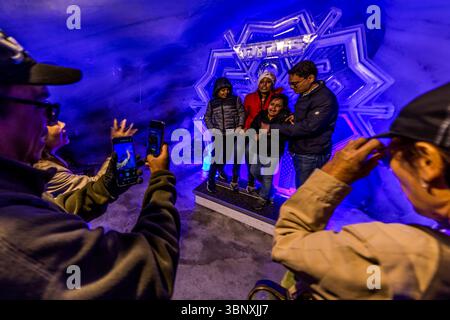 The Titlis glacier grotto is bathed in a mystical turquoise-blue twilight, and the walls are covered with millions of glittering, ancient ice crystals that are up to 5,000 years old. The temperature in the grotto remains a constant frosty minus 1.5 degrees Celsius. Visitors, including a family, pose and take photos of themselves in the impressive, blue-lit ice grotto on the Titlis in Engelberg, Obwalden, Switzerland. The 'TITLIS' ice sculpture serves as a striking backdrop for souvenir photos, while other guests capture the unique atmosphere with their smartphones Stock Photo