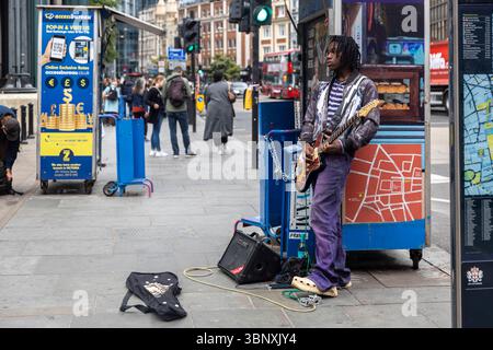 London, UK, 14 May 2025, A young African American man plays an electric guitar on a city sidewalk. Liverpool street Stock Photo