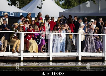 Henley-on-Thames, UK, 4th July 2025. Spectators enjoy the vibrant atmosphere of the Henley Royal Regatta, one of Britain’s most prestigious summer sporting and social events. Visitors dressed in traditional boating blazers, summer dresses, and fascinators line the River Thames to watch the races, cheer on their teams, and celebrate with picnics and champagne. The regatta is known not only for world-class rowing but also for its fashion, people-watching, and quintessentially British charm. Stock Photo