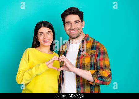 Happy young couple forming a heart shape with their hands against a turquoise background, showcasing love and togetherness Stock Photo