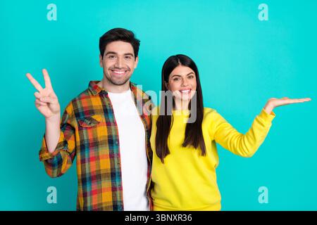 Happy young couple posing against bright turquoise background showcasing love and fun through cheerful gestures and vibrant outfits Stock Photo