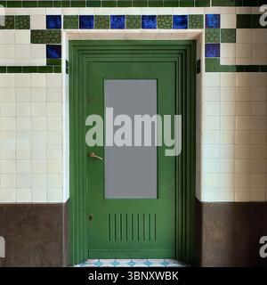 A green side door at Hala Koszyki in Warsaw is framed by tiled walls in green and cobalt, echoing the building’s Art Nouveau roots and market charm. Stock Photo