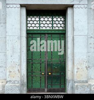 An ornate green metal door in Warsaw features geometric glass inlays and a fan-patterned transom, blending strength and elegance in historic stonework Stock Photo