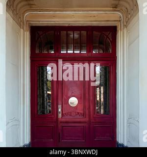 Elegant red Art Deco doorway framed by curved molding and patterned glass panels in central Warsaw. Stock Photo