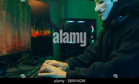 Lviv, Ukraine - June 03, 2024: Masked man anonymous stretching fingers programmer hacking typing computer malware networks web danger scam database Stock Photo