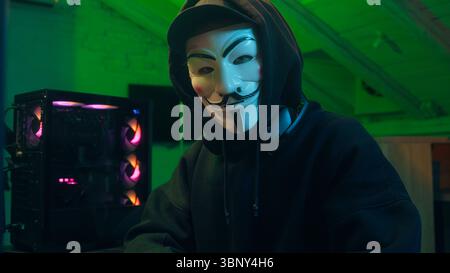 Lviv, Ukraine - June 03, 2024: Hacker anonymous typing computer looking at camera pointing finger programmer attack cyberspace fraud burglar internet Stock Photo