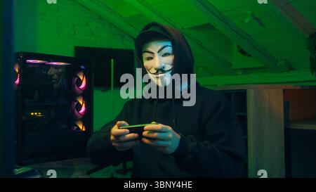 Lviv, Ukraine - June 03, 2024: Man in mask using mobile phone smartphone anonymous looking at camera technology program secure stealing danger banking Stock Photo