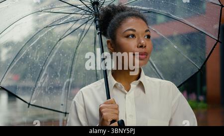 Successful African American woman looking at camera smiling worker holding umbrella rain female girl businesswoman business city leader employer Stock Photo