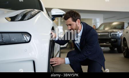 Caucasian man touching checking wheel quality tires new car auto buyer automobile salon test drive rental service choose client male purchase Stock Photo