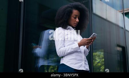African American woman female girl thinking decision pondering urban city user mobile phone smartphone businesswoman business employee chat social Stock Photo