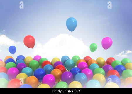 Colorful flat design latex balloons are clustering at bottom against sky with clouds while floating Stock Photo