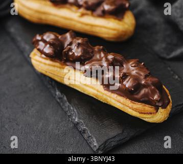 food still-life, Two eclairs with dark chocolate on black board Stock Photo