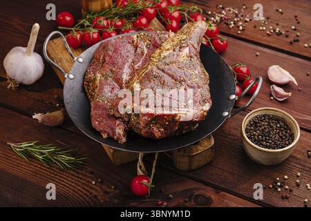 food still-life, Juicy marinated beef steaks are placed on a black skillet, surrounded by garlic, cherry tomatoes, and spices, ready for a flavorful g Stock Photo