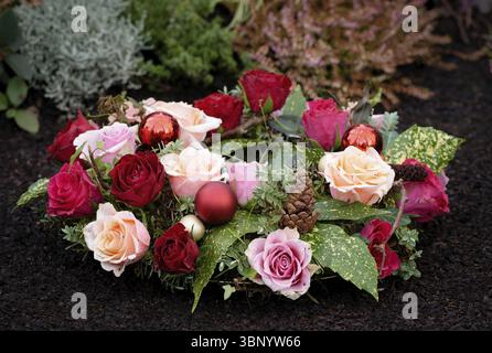 Winter grave arrangement with pink and red roses, christmas tree baubles and pine cones on a well-tended grave Stock Photo
