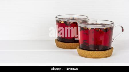 Two cups of berry and flower tea on cork stands on a white table with a copy of the space Stock Photo