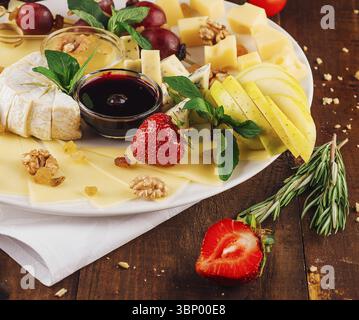 food still-life, Cheese plate presenting variety of cheeses with fruits and nuts on wooden table Stock Photo