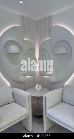 Contemporary Art Installation Featuring Sculpted Faces in a Minimalist Corner with Two Elegant Chairs and a Round Table, Creating an Inviting and Stock Photo