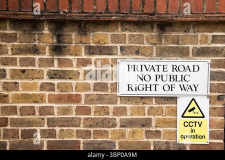 Warning signs mounted on a brick wall: one reading “Private Road No Public Right of Way” above a smaller yellow “CCTV in Operation” Stock Photo