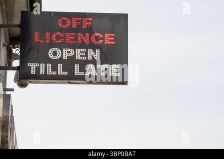 Neon shop sign reading "Off Licence Open Till Late," with red and white text. Although illuminated, the photo was taken in daylight outside the store. Stock Photo