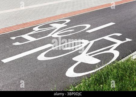 White bicycle lane symbol on urban road. Dedicated cycling path with red curb and greenery. Safe space for eco transport and commuting. Asphalt bike. Stock Photo