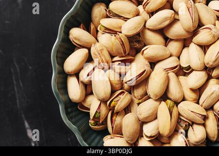 Bowl full of tasty pistachio nuts. Healthy vegetarian snack closeup. Natural organic food rich in protein. Appetizing nuts in decorative bowl on black Stock Photo