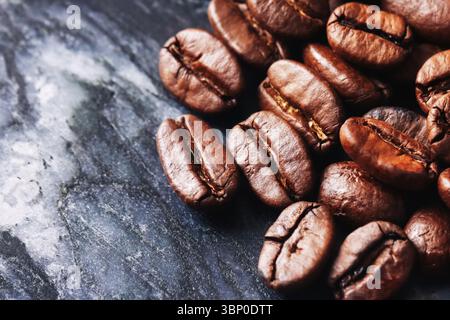 Roasted coffee beans on black stone. Aromatic brown seeds with glossy surface. Natural caffeine ingredient for brewing. Macro texture of espresso. Stock Photo