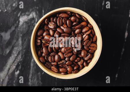 Bowl full of roasted coffee beans. Dark aromatic grains on black background. Natural caffeine source for brewing. High quality macro food texture. Stock Photo