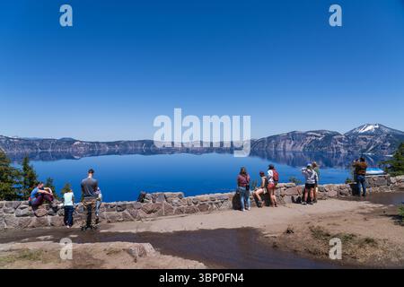 Crater Lake Rim Village South, Oregon, USA - June 17th 2025: Tourists admiring the deep blue water of Crater Lake, early summer, with snow on the rim Stock Photo