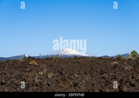 Mount Bachelor, Oregon, USA, viewed from the lava fields of Lava Butte, contrast of the dark lava and the snow covered volcano and volcanic landscape Stock Photo