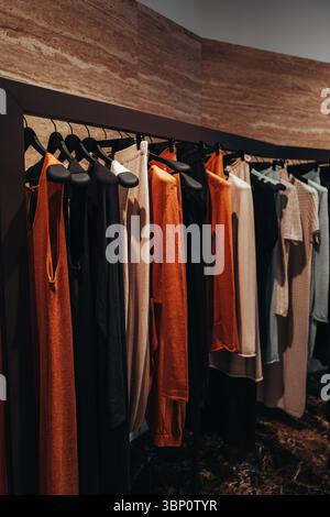 Women's stylish clothes in brown, black and orange colors hanging in a row in a fashionable luxury boutique Stock Photo