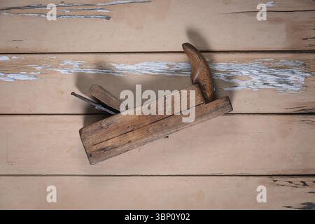 Old wooden hand plane lying diagonally in the center of a worn beige wooden table, photographed from above. Stock Photo