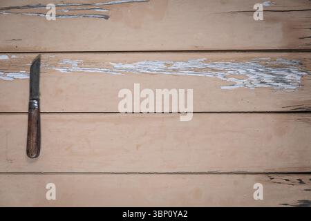 Old folding knife with wooden handle placed on the left edge of a worn beige wooden table. The rest of the frame leaves plenty of empty space for text Stock Photo