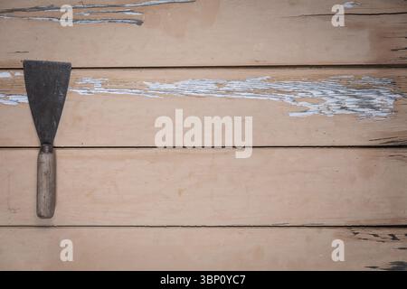 Old putty knife with wooden handle on the left edge of a worn beige wooden table. The rest of the frame leaves empty space fot text or design. Stock Photo