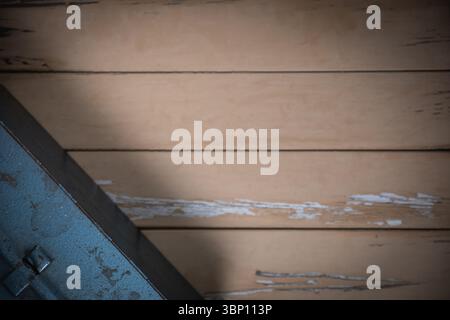 Top-down shot of worn beige wooden table with peeling paint, partial view of old blue metal toolbox in lower left corner, minimalist composition Stock Photo