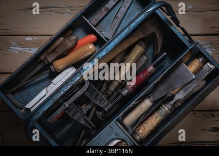 Open blue metal toolbox with vintage tools in compartments on a worn wooden table, showing various old hand tools. Stock Photo