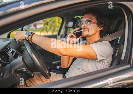 Man with curly hair and sunglasses, drives a car,smokes a cigarette and using phone. Stock Photo