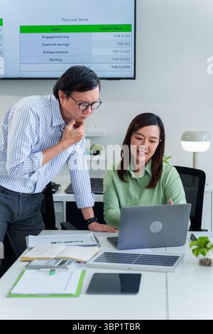 Dedicated Asian businesspeople analyze personal wealth data on a laptop guiding financial planning toward responsible future investments Stock Photo