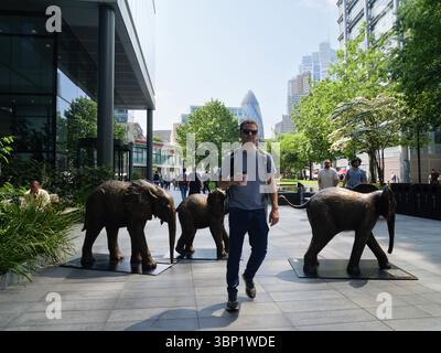 A commuter walks past life-sized bronze elephants from the Herd of Hope installation in Bishops Square, Spitalfields, London, UK — a powerful public art display featuring rescued elephants to raise awareness for elephant conservation Stock Photo