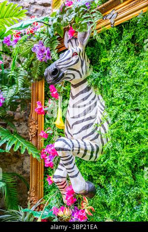 A quirky zebra model emerging from a wall of foliage, part of a colourful floral display with a gilt frame at Leeds Castle, Kent, UK Stock Photo
