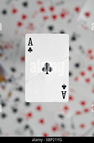 A visibly damaged Ace of Clubs playing card seemingly hovers above a soft, out-of-focus background filled with scattered playing cards Stock Photo
