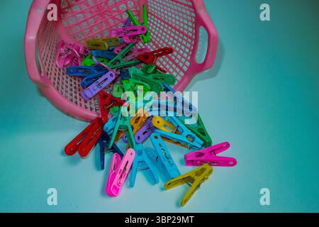 Playful design Plastic clothespins in bright colors scattered from pink basket on light blue background. Everyday household objects in fun design. Stock Photo