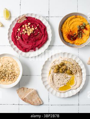 Different types of hummus in bowls and plates. Beetroot, pumpkin ...