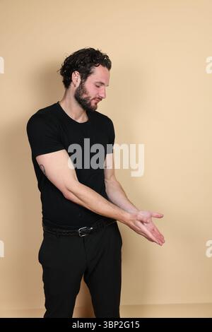 A young man in a black t-shirt and pants looks down towards his hands, which are extended downwards with open palms facing up, as if carefully offerin Stock Photo