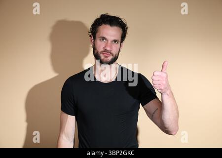 A bearded man with a serious expression, wearing a black t-shirt, gives a thumbs-up gesture directly to the camera, indicating approval or agreement. Stock Photo