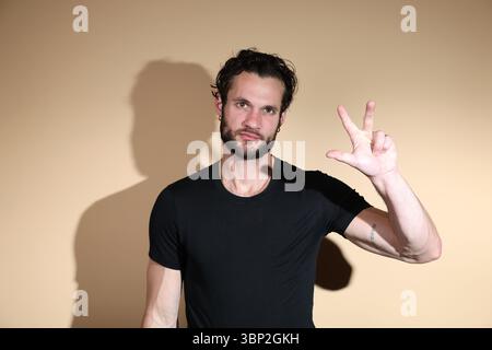 Looking directly at the camera, a bearded man in a black t-shirt holds up three fingers, which could signify the number three, a "W" gesture, or anoth Stock Photo