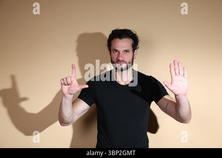 An assertive young man looks directly at the camera, simultaneously making an L-sign with one hand and a clear stop gesture with the other, conveying Stock Photo
