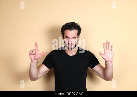 An assertive young man looks directly at the camera, simultaneously making an L-sign with one hand and a clear stop gesture with the other, conveying Stock Photo
